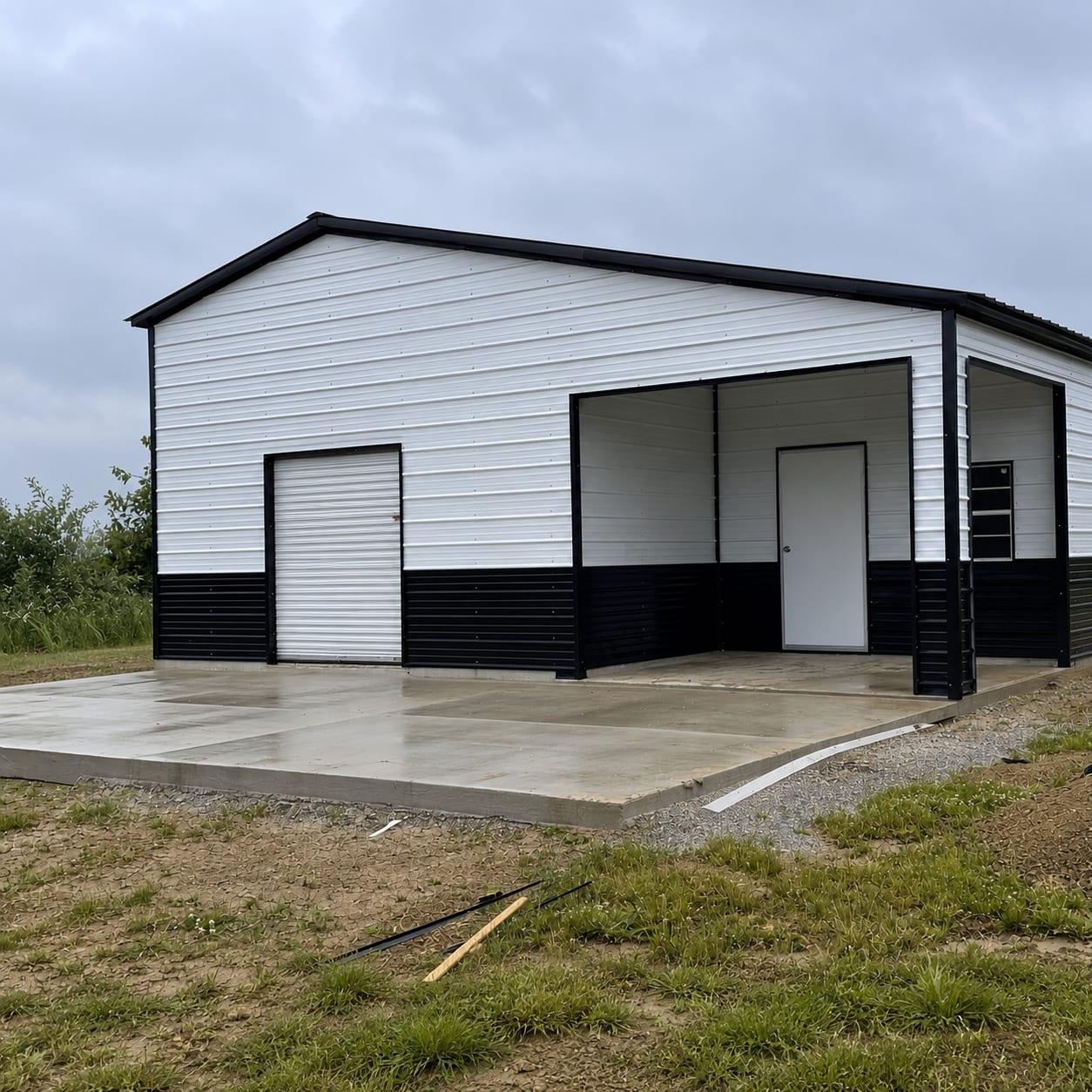 White metal garage with black wainscot and trim, a roll-up door and an open covered bay with a walk-in door