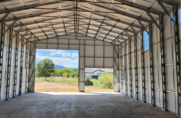 Inside a steel garage looking out through the open end bay toward the hills