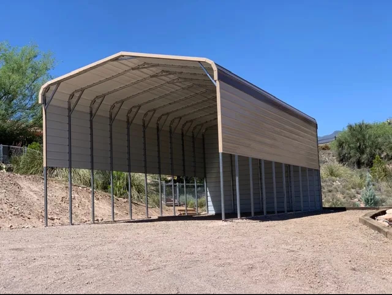 Tall tan metal RV carport with a partly enclosed side on desert ground