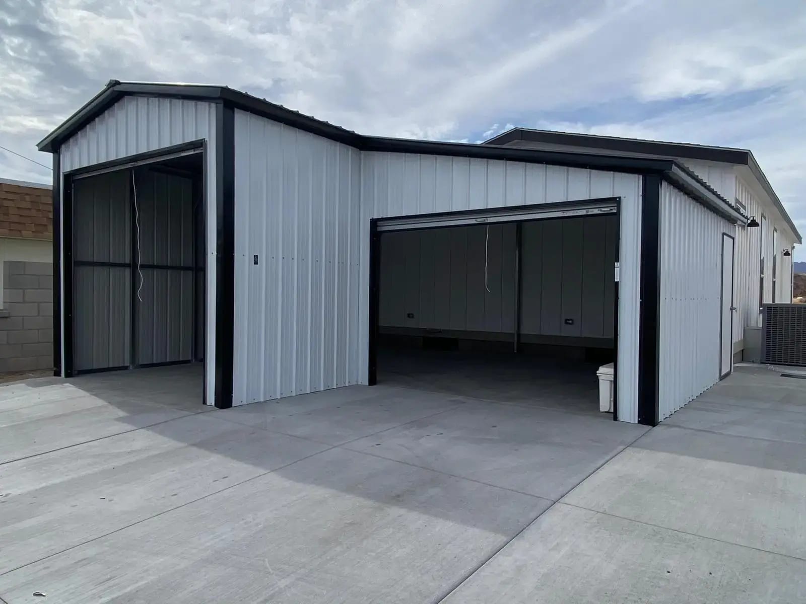 White steel garage with black trim and two open bays on a concrete drive