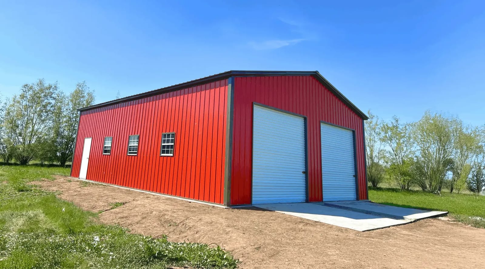 Red metal garage with dark trim, two white roll-up doors, a walk-in door and three windows